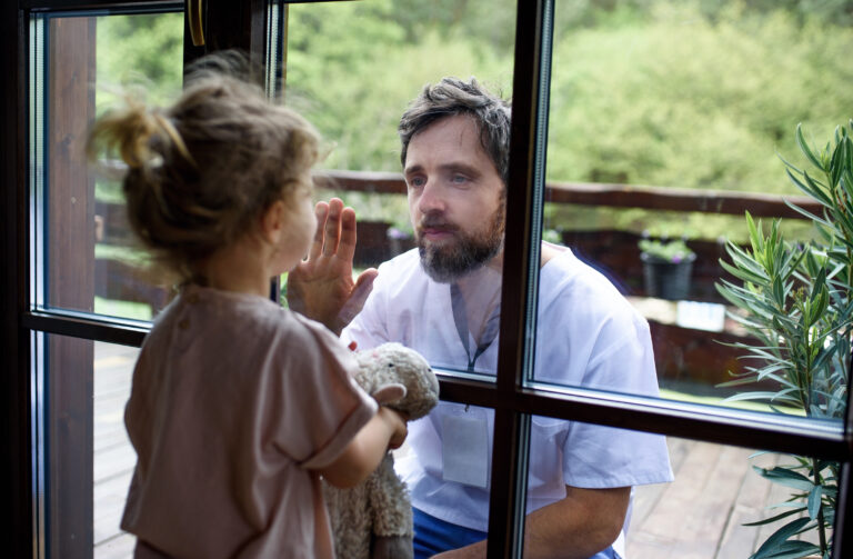 Kind und Vater schauen sich beide an, dabei trennt sie ein Fenster